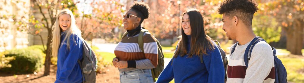 Four students walking on campus in the fall and talking