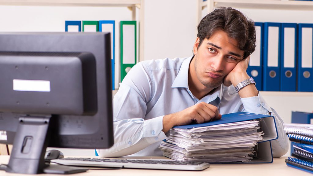 Man with a large stack of paperwork looking sad