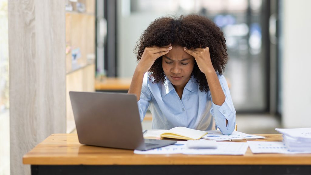 Woman rubbing her temple stressed at a laptop