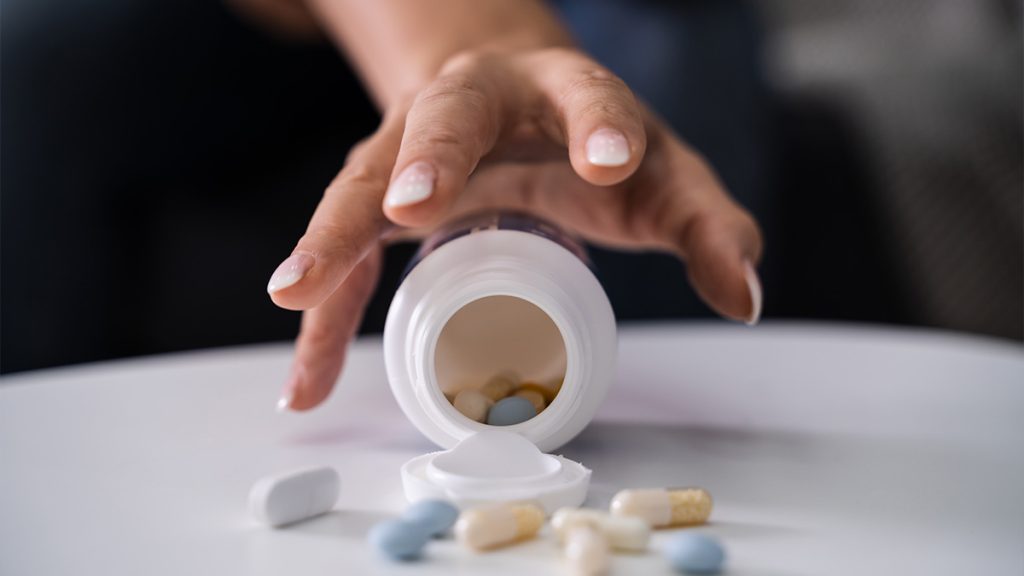 Hand picking up a toppled bottle of pills