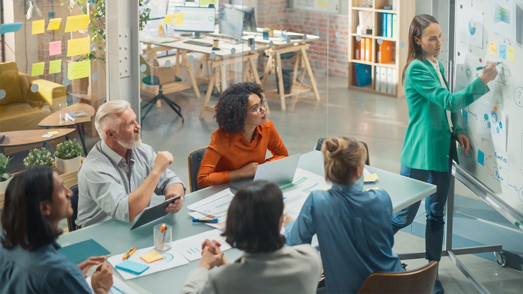 Group discussing at a table with a woman presenting on a board