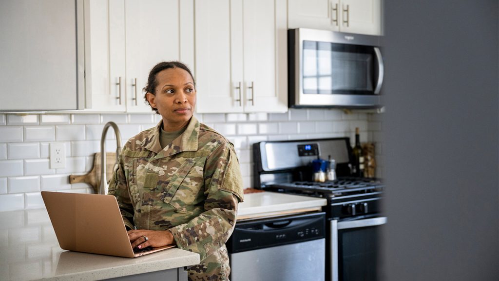 Member of the army in a kitchen on a laptop