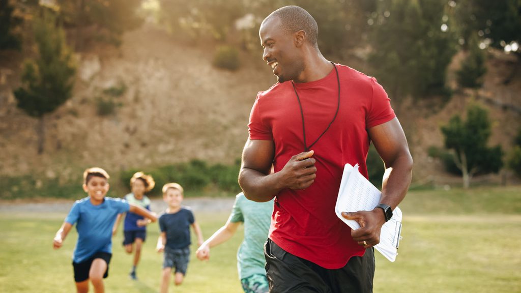 Image of a coach in red shirt with young soccer players running behind him