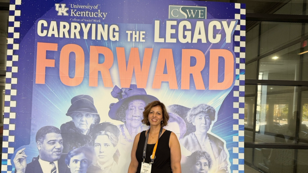 Brillon stands in front of College of Social Work and CSWE backdrop with "Carrying the Legacy Forward" written over top of multiple social work legends photos