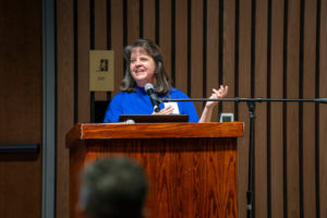 Debbie Carey speaking at a podium with her hand raised.