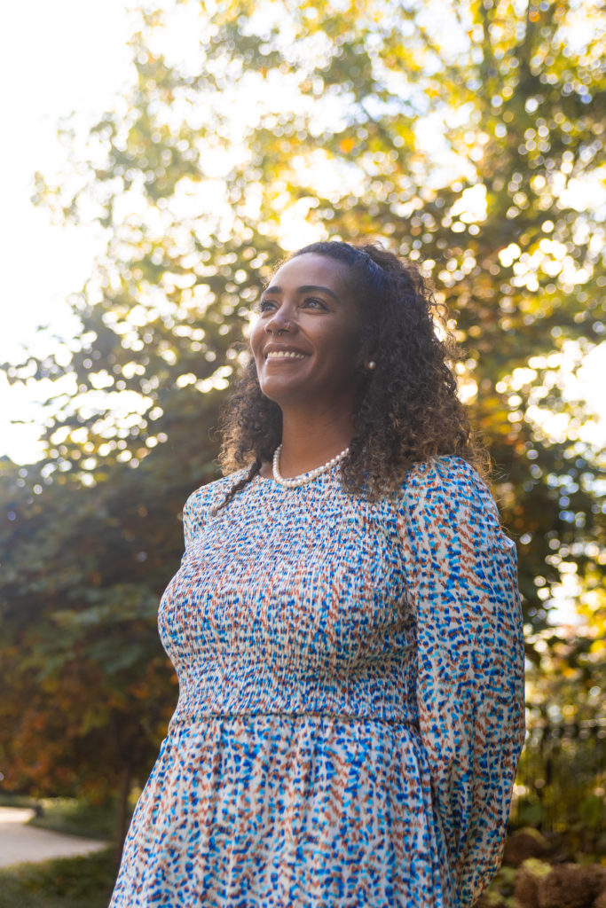 Image of Dr. Laneshia Conner smiling and looking up into the sky, arms crossed behind her back, with blue floral patterned dress and pearl necklace