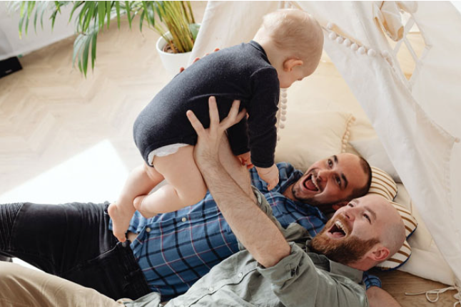 Two men lying on the floor smiling and playing with a baby