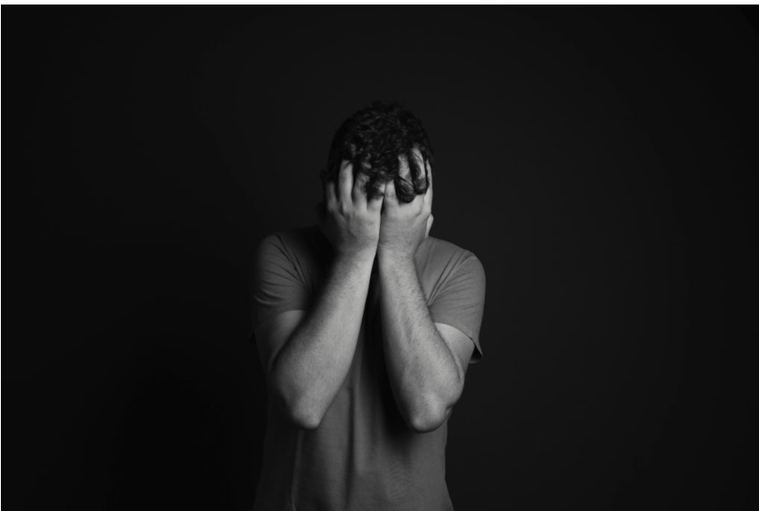 Black and white image of a man covering his face with his hands