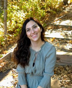 Image of Ally Meisner sitting in a wooded area smiling at the camera