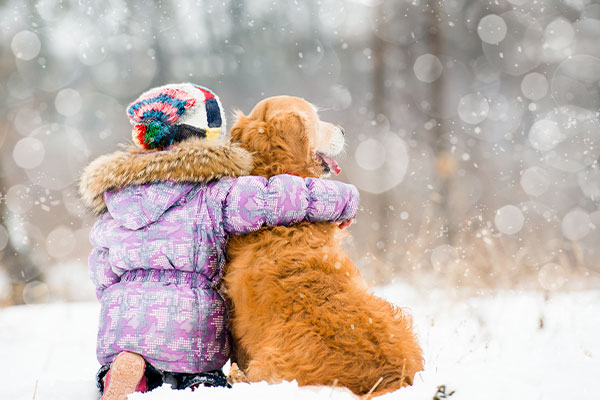Girl in winter coat hugging a dog outside in the snow