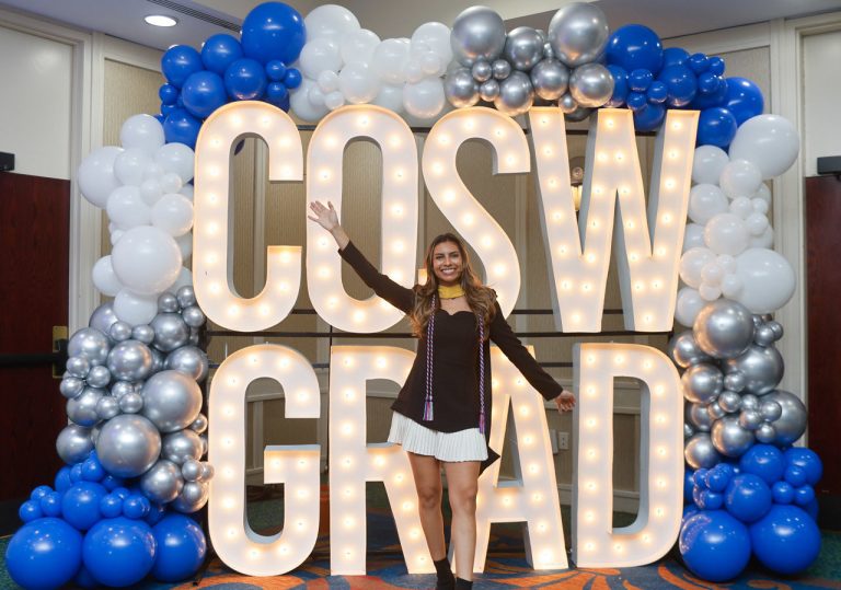Graduate standing in front of a lighted CoSW Grad sign