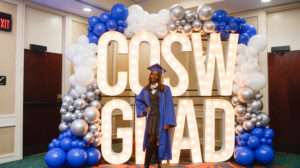 Ta'Niya Rucker stands in front of "COSW GRAD" lights