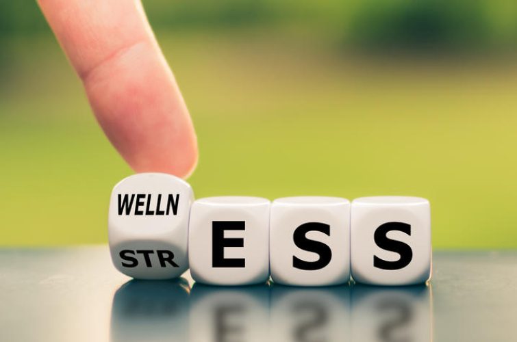 Wellness instead of stress. Hand turns a dice and changes the word "stress" to "wellness".